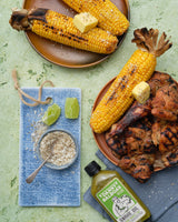 Danny Balboa's SNAKE OIL - Jalapeno, Pineapple + Lime Hot Sauce, 200ml bottle, lying on a table next to a plate of jerk chicken and corn cobs