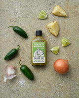 Danny Balboa's SNAKE OIL - Jalapeno, Pineapple + Lime Hot Sauce, 200ml bottle, lying on a table surrounded by the fresh ingredients which the sauce is made of.