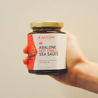 A hand holding a jar of Kansom Australia Abalone Hot Chilli Sea Sauce.