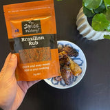 The Spice Factory Brazilian Rub Mix packet held above a plate of meat coated in the rub.