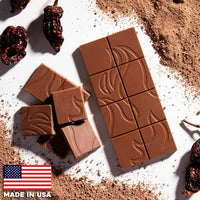 Flamethrower Candy's Ghost Pepper Chocolate bar, unwrapped, with a pattern, surrounded by cocoa powder and dried fruits on a white background, with 'Made in USA' label.