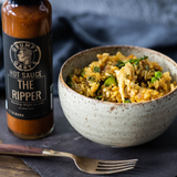 A 245ml bottle of Grumpy Gary's The Ripper Hot Sauce beside a bowl of stirfry.