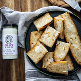 Plated bread slices with a jar of Grumpy Gary's Gar-Lick Dip on a wooden surface