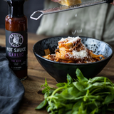 Bowl of pasta with a bottle of Grumpy Gary's Garlic Hot Sauce on a wooden table.