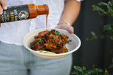 Person pouring Grumpy Gary's Mango hot sauce over a bowl of food.