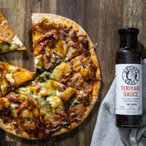 Pizza with a bottle of Grumpy Gary's Teriyaki Sauce on a wooden surface