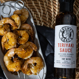 Bottle of Grumpy Gary's Teriyaki Sauce next to skewers of marinated shrimp.