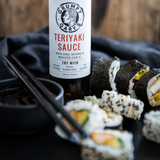 Bottle of Grumpy Garry's Teriyaki Sauce with sushi rolls on a dark surface