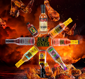 An assortment of Hot Ones hot sauces displayed in a circle with their bottles facing forward. Each sauce has a different colour label and appearance, and they are presented with a backdrop of a fiery, smoky hot sauces and chicken wings.