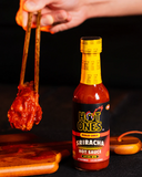 Hot Ones Pickled Garlic Sriracha hot sauce bottle with a piece of fried chicken being held by a pair of chopsticks against a dark background - buy online Australia | Blonde Chilli