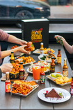 People enjoying a meal with various dishes and Hot Ones branded products on a table.