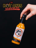 A 148ml bottle of Microsaucerie Piko Peppers Garlic Delight Hot Sauce being held by the neck of the bottle on a black background.