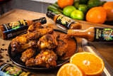Three bottles of Sauce Leopard Homegrown Hell Sichuan Tangerine Hot Sauce laying on a table around a plate of hot wings.