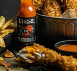 Bottle of 13 Angry Scorpions' The Notorious Hot Sauce with fried chicken and fries on a dark surface