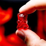 Red gummy bear held between two fingers against a blurred red background