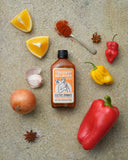 Danny Balboa's ELECTRIC DYNAMITE - Capsicum, Orange and Habanero Hot Sauce, lying on a table surrounded by fresh ingredients as found in this hot sauce