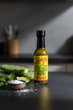 A bottle of Jibbas Nopale Verde on a kitchen benchtop beside some green nopales and coriander.