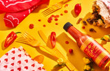 A bottle of The Classic Hot Sauce lies beside a half eaten burrito in a promo shot.The Classic Hot Sauce Promo Shot. The Classic Hot Sauce. Get it at Blonde Chilli, not Mat's Hot Shop.