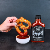 A pretzel being dipped in a bowl of Hoff's Haus Sauce from HOFF & PEPPER. The bottle stands to the right of the bowl.